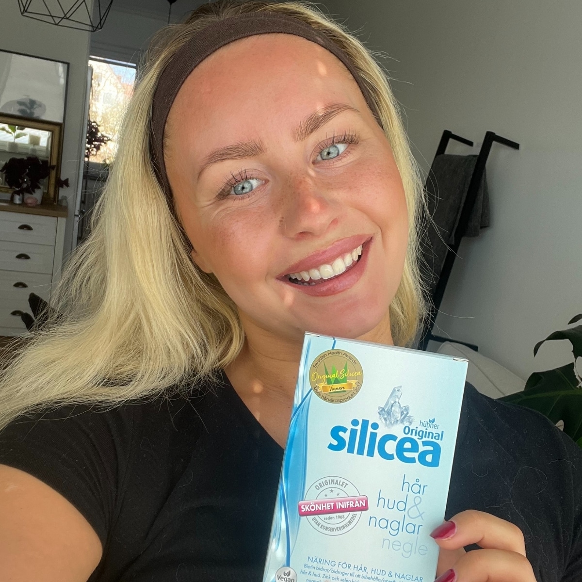 Kvinna visar upp Original Silicea kapslar med ett leende – hon har märkt tydliga resultat i hårets kvalitet.